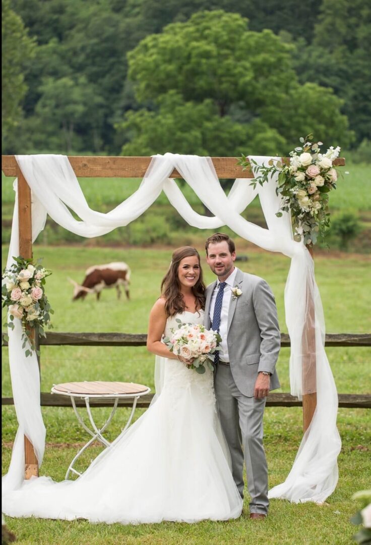 A bride and groom pose for a picture in front of their wedding arch.