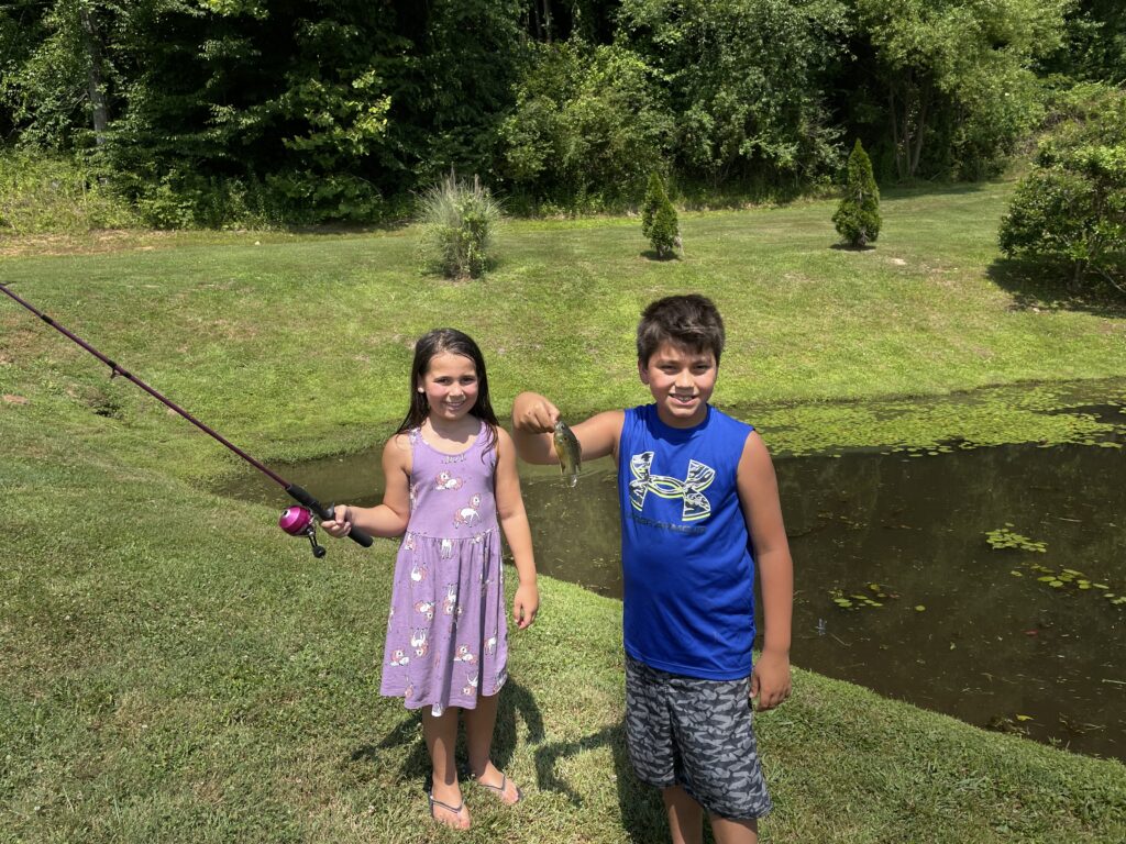A boy and girl are fishing in the grass.