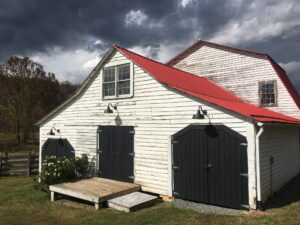 A white barn with black doors and red roof.