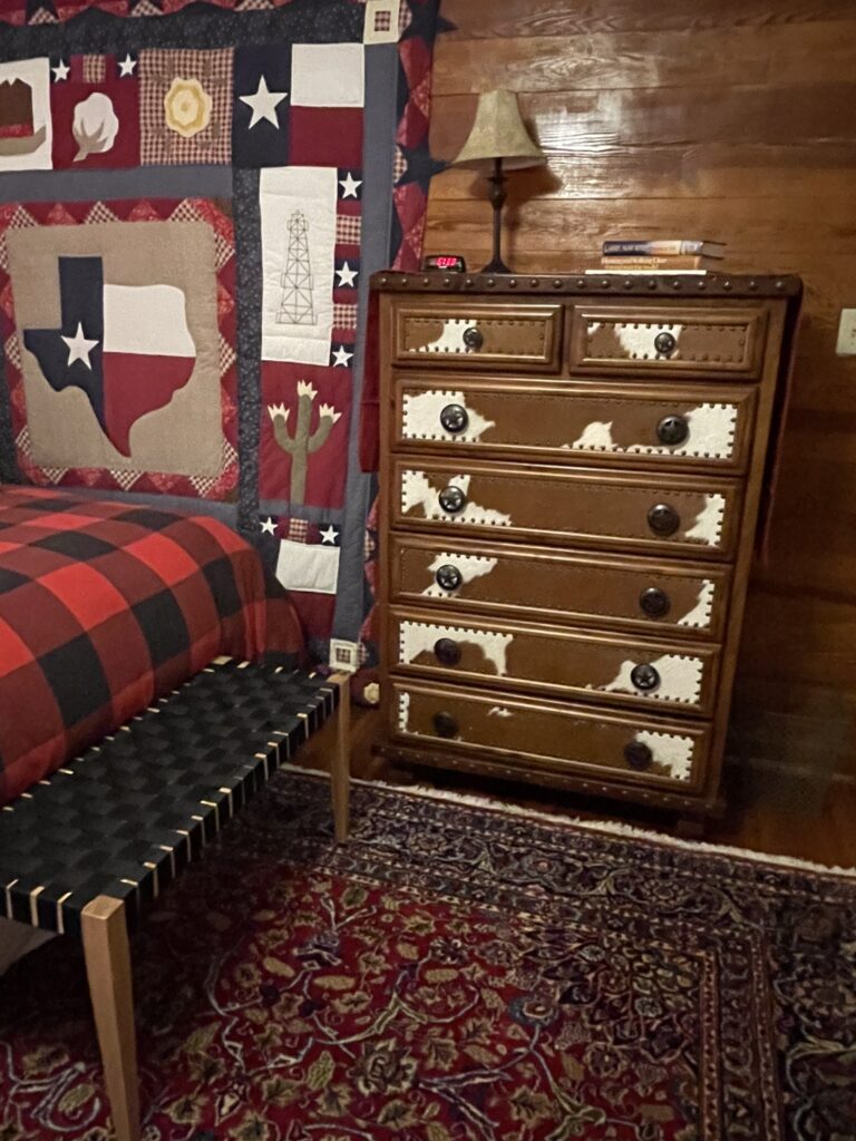 A dresser in the corner of a room with a bed.