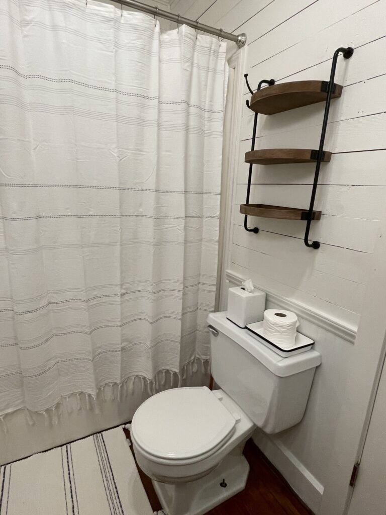 A bathroom with white walls and wooden shelves.